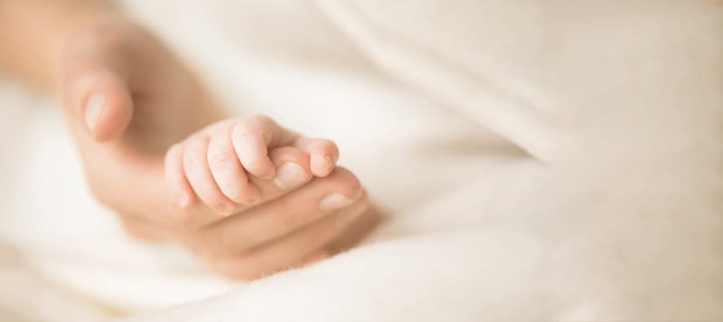 Female hand holding her newborn baby's hand. Mom with her child. Maternity, family, birth concept