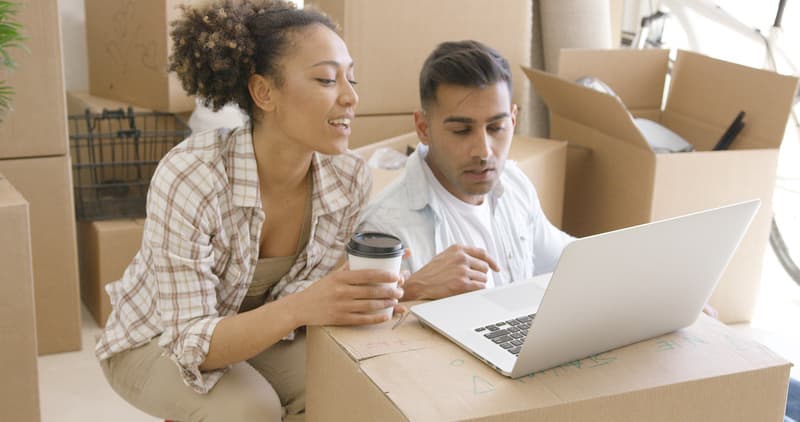 Young mixed race couple sitting on the floor of new home they just moved in. They using laptop for planning.