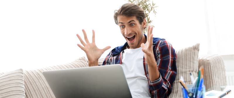 surprised young man with laptop sitting on sofa