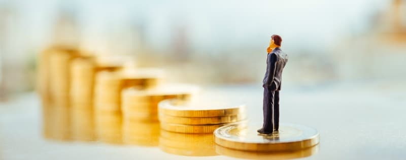Miniature people: small figure businessman standing on a stack of coins with city background. Money, Financial, Business Growth concept.