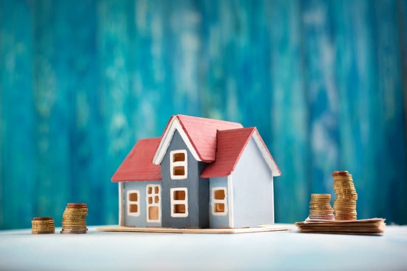 Red house model on wooden background with banknotes and coins